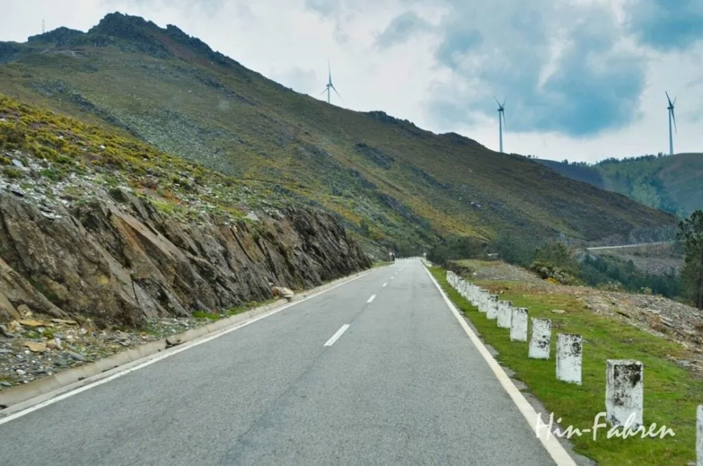 Straße durch karge Berge in Nord-Portugal, auf dem Bergkamm stehen Windräder