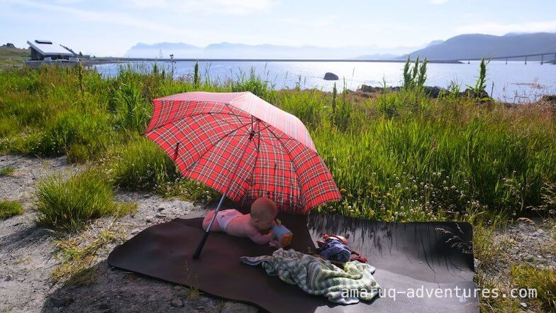 Baby unter einem Schirm, im Hintergrund das Meer