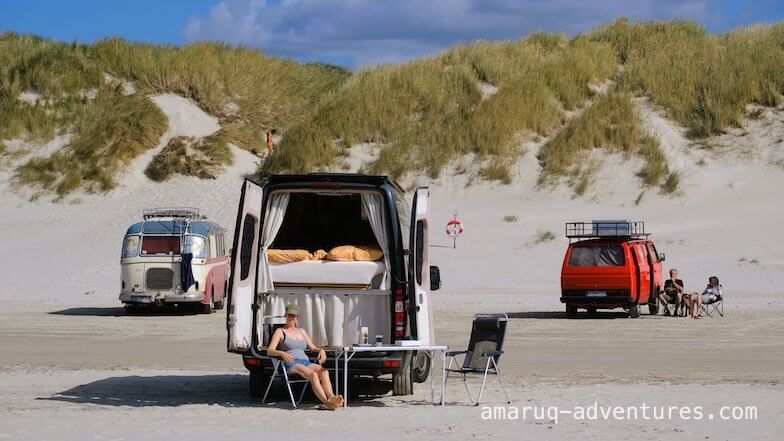 Frau sitzt vor einem Camper, der auf dem Strand steht
