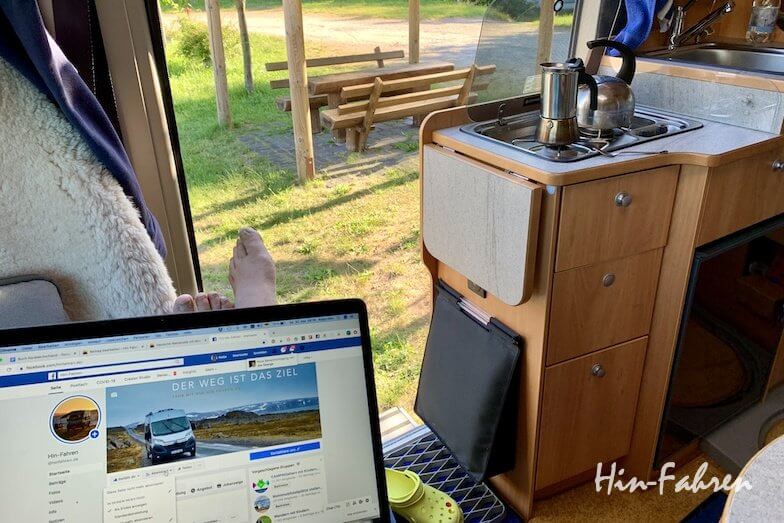 Aufgeklapptes Laptop im Inneren eines Wohnmobils mit Blick aus der Schiebetür