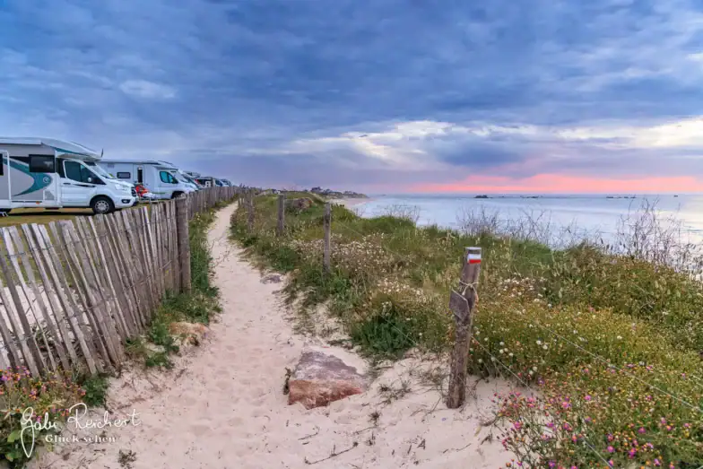 Ein Weg mit einem Zaun und Gras und ein Strand mit geparkten Wohnmobilen