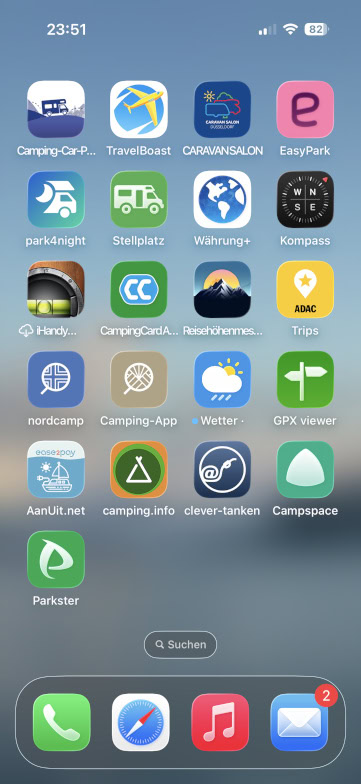 Screenshot eines Smartphone-Startbildschirms mit verschiedenen Camping-, Reise- und Navigations-Apps, darunter Karten, Buchungs-, Wetter- und Benzinpreis-Apps, die in einem Raster vor einem unscharfen blauen Hintergrund angeordnet sind. Die Uhrzeit ist 23:51.