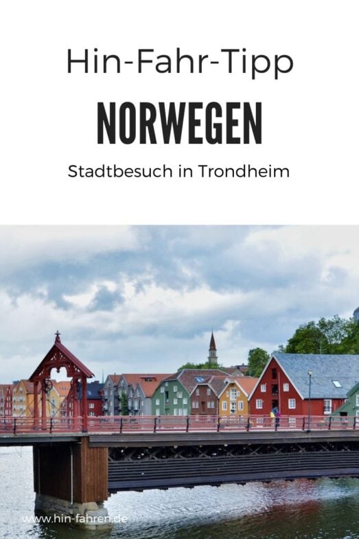 Bunte Holzhäuser säumen einen Fluss in Trondheim, Norwegen, mit einer roten Brücke im Vordergrund und einem bewölkten Himmel darüber. Der Text auf dem Bild enthält Reisetipps für die Erkundung von Trondheim mit dem Wohnmobil.