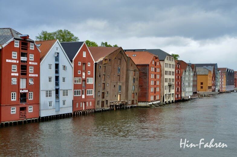 Farbenfrohe Holzhäuser mit steilen Dächern säumen einen Fluss in Trondheim.