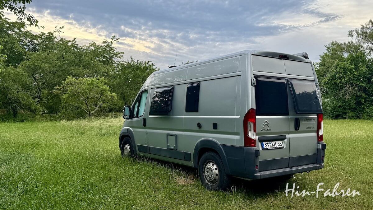 Ein silberner Citroën-Kastenwagen steht auf grünem Gras in der Nähe von Bäumen unter einem bewölkten Himmel. Das Bild trägt in der rechten unteren Ecke den Schriftzug „Hin-Fahren“. Es ist Katjas bester Kastenwagen.