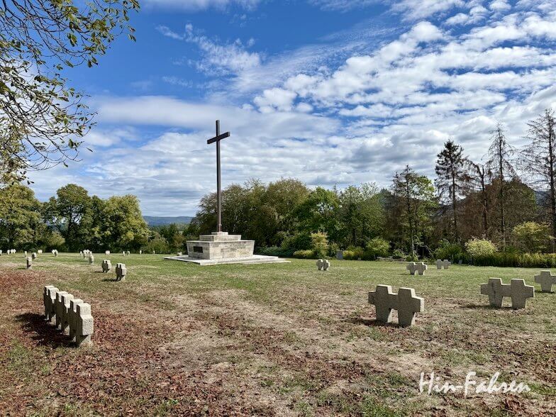 Inmitten von Reihen kleiner, kreuzförmiger Grabsteine steht auf einem grasbewachsenen Friedhof in der Nähe des Wohnmobilstellplatzes an der Hohenzollernstraße ein hohes Steinkreuz.