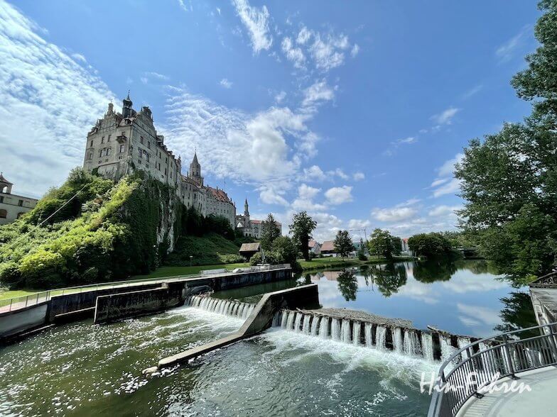 Eine Burg auf einem felsigen Hügel mit Blick auf einen Fluss mit einem Stufenwehr, gesehen vom Wohnmobilstellplatz an der Hohenzollernstraße aus.
