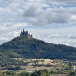Das Schloss Hohenzollern thront unter bewölktem Himmel auf einem bewaldeten Berggipfel und ist ein Stop auf der Hohenzollernstraße mit Wohnmobil.
