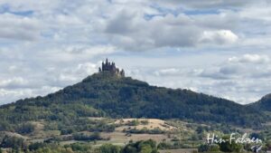 Das Schloss Hohenzollern thront unter bewölktem Himmel auf einem bewaldeten Berggipfel und ist ein Stop auf der Hohenzollernstraße mit Wohnmobil.