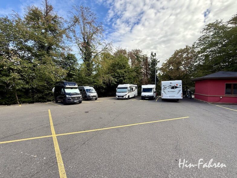 Vier Wohnmobile standen auf einem asphaltierten Parkplatz in der Hohenzollernstraße, umgeben von Bäumen.