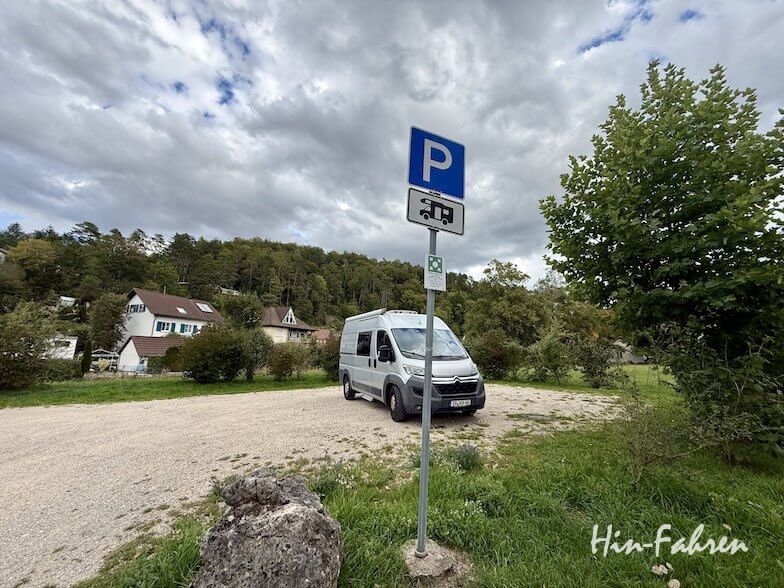 Ein silberner Wohnwagen, der auf einem Wohnmobilstellplatz in der Hohenzollernstraße neben einem Schild mit der Aufschrift „Wohnmobilparkplatz“ geparkt war.